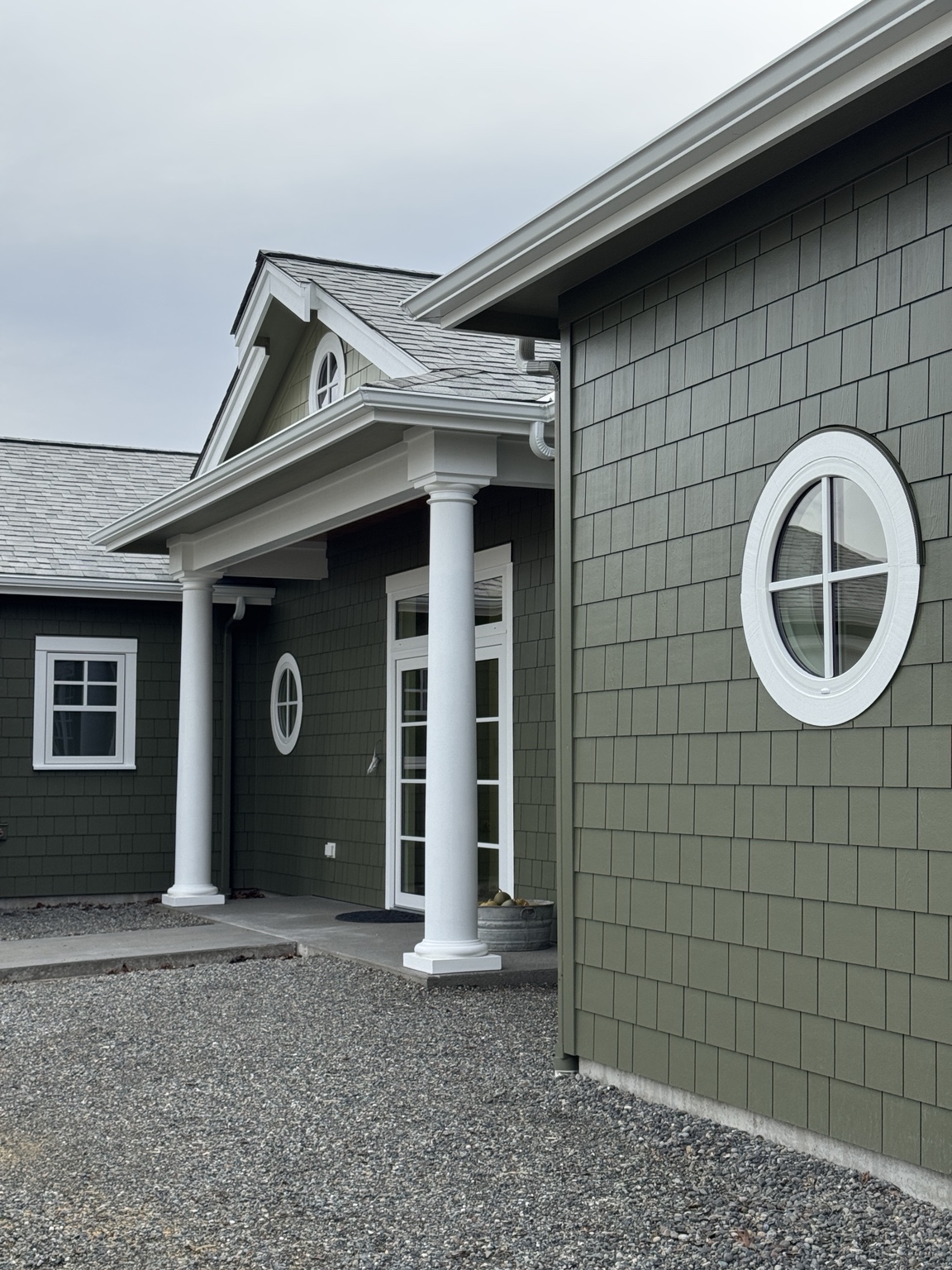 Front entry with green shingles, white trim, and round window